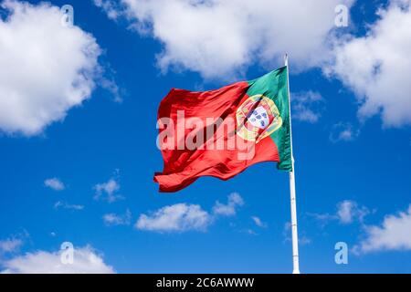 Portugiesische Nationalflagge winkt im Wind gegen blauen sonnigen Himmel mit weißen Wolken, Portual Stockfoto