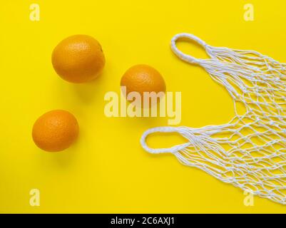 Weiße Baumwollsaite Öko-Beutel und drei Orangen auf gelbem Hintergrund. Einfache, flache Verlegung. Ökologie Null Abfall Konzept. Stock Foto. Stockfoto