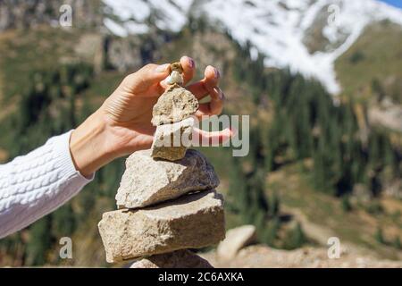 Cairn auf dem Hintergrund verschneiter Berge. Frau Hand legt einen Stein Stockfoto
