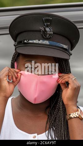 England, Großbritannien. 2020. Porträt einer Frau Chauffeur mit Uniform Kappe und geflochtenen Haaren Anpassung ihrer rosa gefärbten Gesichtsmask während der Covid-19 Ausbruch Stockfoto