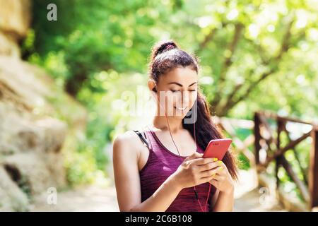 Schöne Mädchen Athlet wählt einen Track in einem Smartphone. Porträt eines schönen Sportmodels im Park mit einem Telefon in der Hand Stockfoto