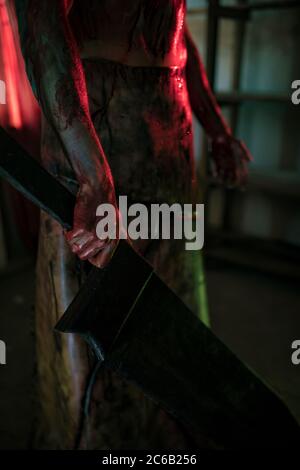 Cosplayer im Bild des Henkers steht im dunklen Raum in Schürze mit Messer in der Hand. Nahaufnahme. Stockfoto