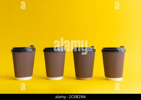 Vier braune togo Kaffeetassen mit schwarzen Bezügen auf gelbem Hintergrund, Stockfoto