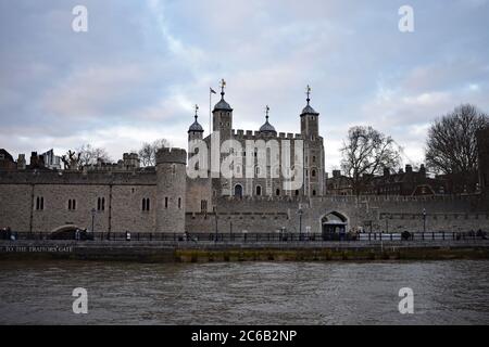 Fußgänger gehen an einem Over Cast Day am Tower of London vorbei. Der Weiße Turm erhebt sich vom Schlossgelände entlang des nördlichen Ufers der Themse. Stockfoto