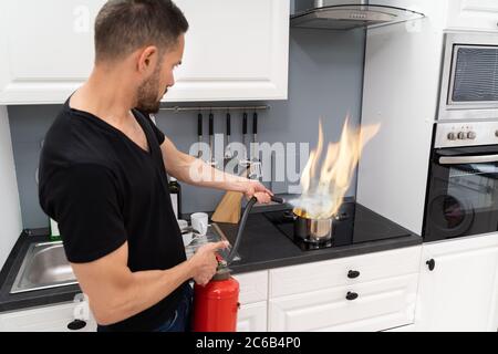 Mann mit Feuerlöscher zu stoppen Feuer zum Brennen von kochenden Topf in der Küche Stockfoto