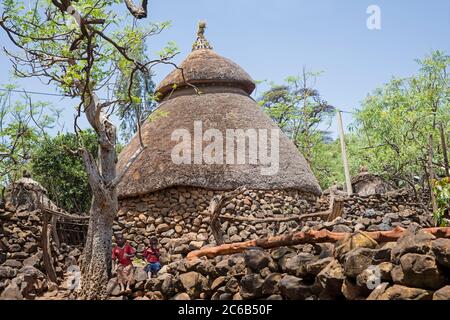 Zwei schwarze Kinder vor der traditionellen Steinhütte mit Reetdach des Konso / Xonsita Stammes, Süd-West Äthiopien, Afrika Stockfoto