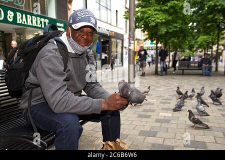 Glasgow, Schottland, Großbritannien. Juli 2020. Im Bild: Ein Mann füttert Tauben von Hand in der Sauchielhall Straße im Glasgows Einkaufsviertel. Quelle: Colin Fisher/Alamy Live News Stockfoto