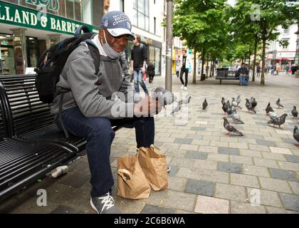 Glasgow, Schottland, Großbritannien. Juli 2020. Im Bild: Ein Mann füttert Tauben von Hand in der Sauchielhall Straße im Glasgows Einkaufsviertel. Quelle: Colin Fisher/Alamy Live News Stockfoto