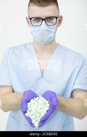 Junge medizinische Arbeiter trägt Brille und Schutzmaske hält eine Handvoll Pillen Stockfoto