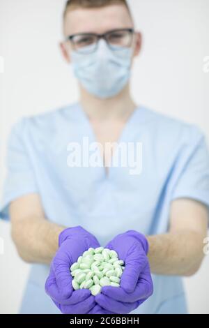 Junge schöne Praktikant trägt Brille und Schutzmaske hält eine Handvoll Pillen Stockfoto
