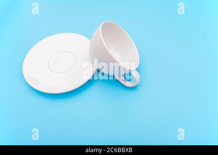 Umgedreht oder umgestoßen leere weiße Kaffeetasse, Tasse mit Schale auf blauem Hintergrund, Konzeptbild Stockfoto