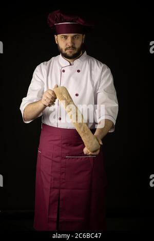 baker Mann trägt violette Schürze und Kappe hält Baguette Brot isoliert auf schwarz Stockfoto
