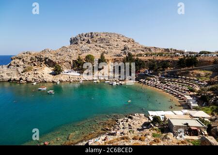 Sonnenschirmen säumen den Strand an der St. Paul's Bay an einem sonnigen Tag in Lindos auf Rhodos, Dodekanes, griechischen Inseln, Griechenland, Europa Stockfoto