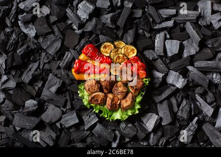 Shish Kebab und gegrilltes Gemüse - Paprika, Zucchini, Kirsche, Tomaten auf einem runden Teller. Dunkelgrauer Hintergrund. Stockfoto