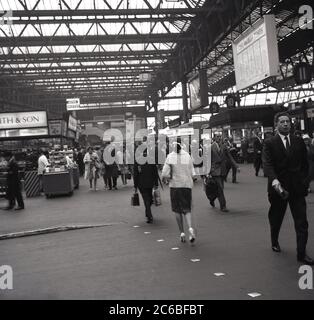 1960er Jahre, historisch, Zugpassagiere auf der Bahnhofshalle an der Waterloo Station, South London, England, Großbritannien. Das Bild zeigt gut gekleidete Menschen, die an Verkaufsständen vorbeilaufen. Schilder für „Auto Buffet“ und „Cartoon Cinema“ sind zu sehen. Stockfoto