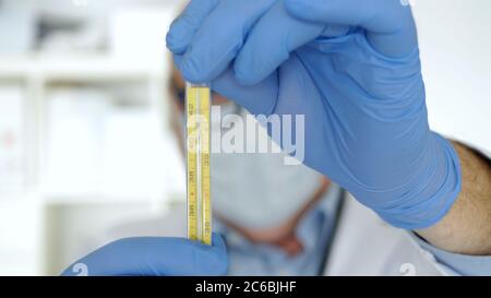 Arzt mit Schutzhandschuhe und Gesichtsmaske Halten in der Hand ein medizinisches Thermometer zur Kontrolle der menschlichen Körpertemperatur verwendet Stockfoto