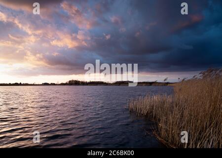 Dunkle Wolken nach Sonnenuntergang am See mit Schilf Stockfoto