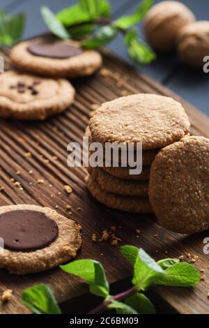 Gesunde zuckerfreie glutenfreie vegetarische Süßigkeiten. Erdnussbutter-Kekse mit dunklen Schokoladentropfen serviert mit roher Minze auf dunklem Eichenbrett Hintergrund Stockfoto