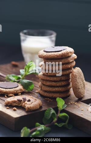 Vegetarische Süßigkeiten für gesunde Snacks. Erdnussbutter und Mandelgebäck mit Schokoladentropfen serviert in Haufen mit Pflanzenmilch und Minze auf dunklem Eichenbrett c Stockfoto