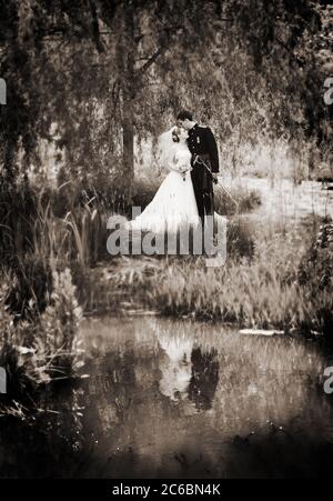 Zauberhaftes Märchenhochzeit-Foto mit Prinz & Prinzessin-Feeling. Braut & Bräutigam in Militärkleidung Uniform mit Schwert im See reflektiert. Sepia getönte. Stockfoto