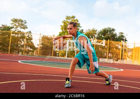 Basketball. Ein Teenager in grüner Sportkleidung spielt Basketball. Im Hintergrund ist ein Sportplatz. Speicherplatz kopieren. Konzept der Sportspiele. Stockfoto