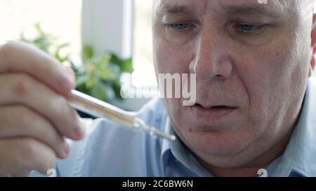 Mann mit Coronavirus-Symptomen, der seine Körpertemperatur in einem Krankenhaus mit einem Thermometer mit Quecksilberskala einnahm Stockfoto