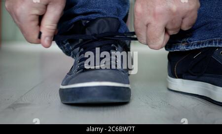 Mann, der sich auf einen Spaziergang vorbereitet und die Schnürsenkel an seine Sportschuhe bindet Stockfoto