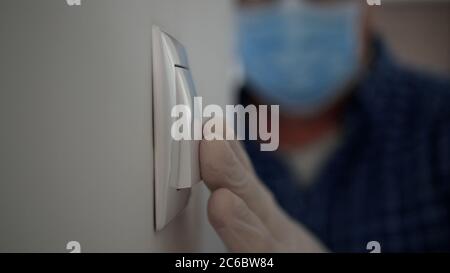 Mann trägt medizinische Maske und Schutzhandschuhe Betreten Sie den Büroraum und schalten Sie das Licht aus dem Schalter, Arbeitsplatz Quarantäne in Pandemie. Stockfoto