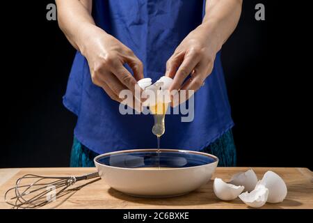 Eine Frau bricht auf und Ei und das Eigelb fällt in die Schüssel. Stockfoto
