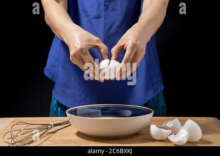 Frau knackt ein Ei, um es in eine Rührschüssel zu geben. Stockfoto