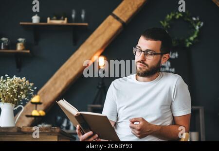 Junger Kaukasischer bärtiger Mann liest in der Küche ein Buch. Freizeit zu Hause. Stockfoto
