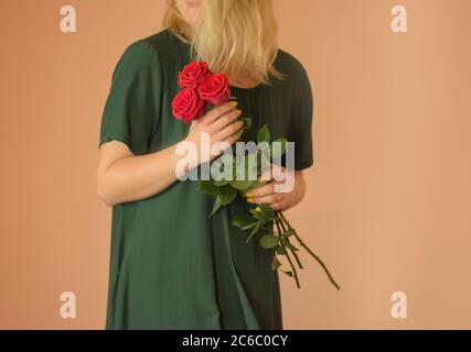 Mädchen mit Strauß von roten Rosen. Frühlingsstrauß von roten Rosen in Frauenhand auf hellbeigem Hintergrund Stockfoto