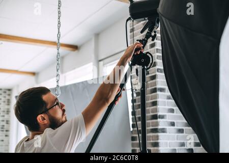 Junger Kaukasischer passt Beleuchtungsausrüstung in einem Fotostudio an. Stockfoto