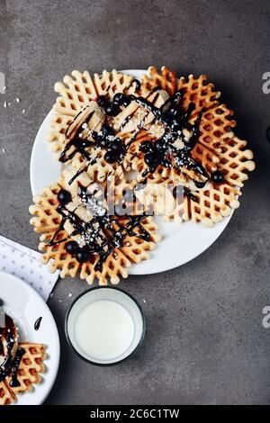 Hausgemachte Waffeln mit Schokolade, Banane und Beeren auf einem weißen Teller. Stockfoto