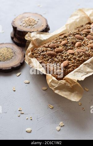 Hausgemachte glutenfreie zuckerfreie vegetarische Snack. Haferflockenbrot in Papier gebacken serviert mit ganzen Mandeln, Flachs und Amaranth Samen auf Holzplatten auf Whi Stockfoto