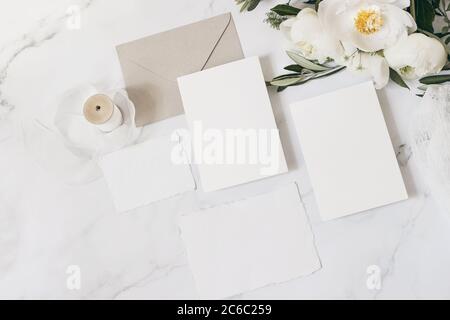 Hochzeitsbriefpapier, Stillleben Komposition. Grußkarten Mockup Szene. Bouquet von weißen Pfingstrosen Blumen, Olivenzweige, Kuh Petersilie auf Marmortisch Stockfoto