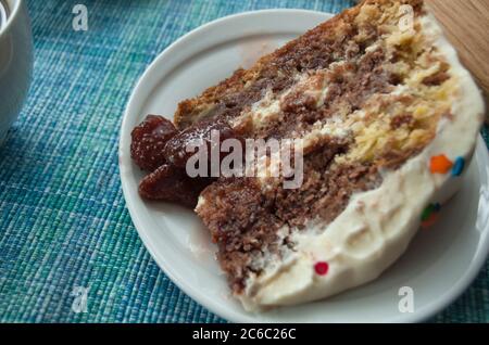 Ein Stück Schokoladenkuchen mit Sahne auf einem weißen Teller close up mit bunten Belag und einer Tasse Kaffee dekoriert Stockfoto