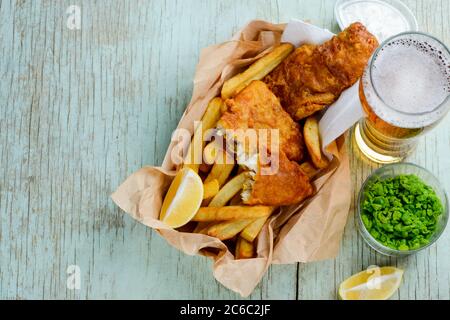 Frittierter Fisch und Pommes mit Zitronenscheiben, grünen Erbsen und Bier Stockfoto