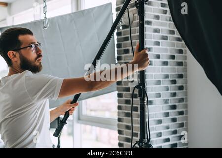 Junger Kaukasischer passt Beleuchtungsausrüstung in einem Fotostudio an. Stockfoto