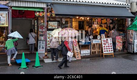 Menschenmenge, die an einem regnerischen Tag in Tokio, Japan, um die kleine schmale Straße des Tsukiji Outer Market schlendern Stockfoto