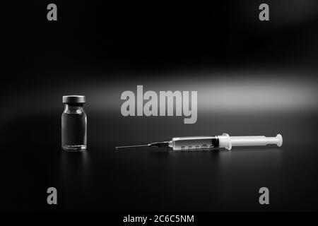 Kleine Impfstoffflasche (Fläschchen) und eine medizinische Spritze Injektion mit einem Impfstofftropfen auf seiner Nadel, isoliert auf schwarzem Hintergrund Impfung für preventio Stockfoto