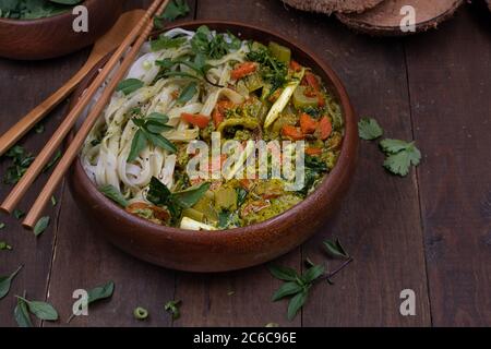 Veganes Thai Green Curry und Reisnudeln in Holzschüssel auf Holztisch serviert Stockfoto