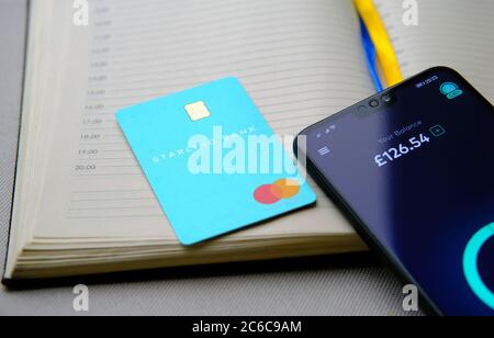 Stone / UK - 8. Juli 2020: Starling Bankkarte auf Tagebuch und Smartphone platziert mit Starling App zeigt das Gleichgewicht auf dem Bildschirm. Stockfoto