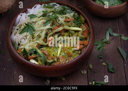 Veganes Thai Green Curry und Reisnudeln in Holzschüssel auf Holztisch serviert Stockfoto