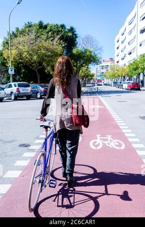 Rückansicht einer lächelnden Frau, die mit dem Fahrrad auf einer Stadtstraße läuft Stockfoto