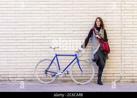 Junge Frau, die an sonnigen Tagen mit einem Vintage-Fahrrad an einer Stadtmauer angelehnt ist Stockfoto