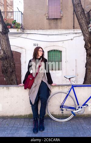 Junge Frau, die an sonnigen Tagen mit einem Vintage-Fahrrad an einer Stadtmauer angelehnt ist Stockfoto