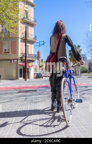 Rückansicht einer lächelnden Frau, die mit dem Fahrrad auf einer Stadtstraße läuft Stockfoto