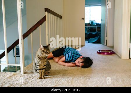 Boy legt sich auf den Boden der Treppe als nächstes Zu seiner tabby Katze Stockfoto