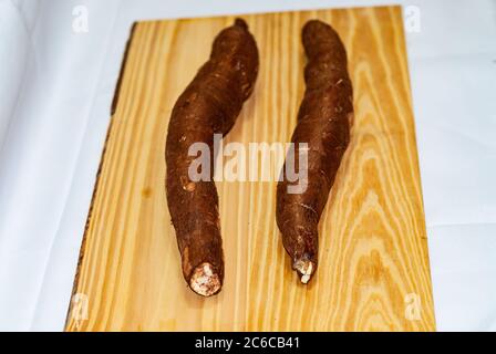 Rohe Yucca auf dem Holztisch, Manihot esculenta. (Cassava roh Knolle). Maniok, auch Mandioca, Yuca, Balinghoy, mogo, Mantoca, kamoteng kahoy genannt, Stockfoto